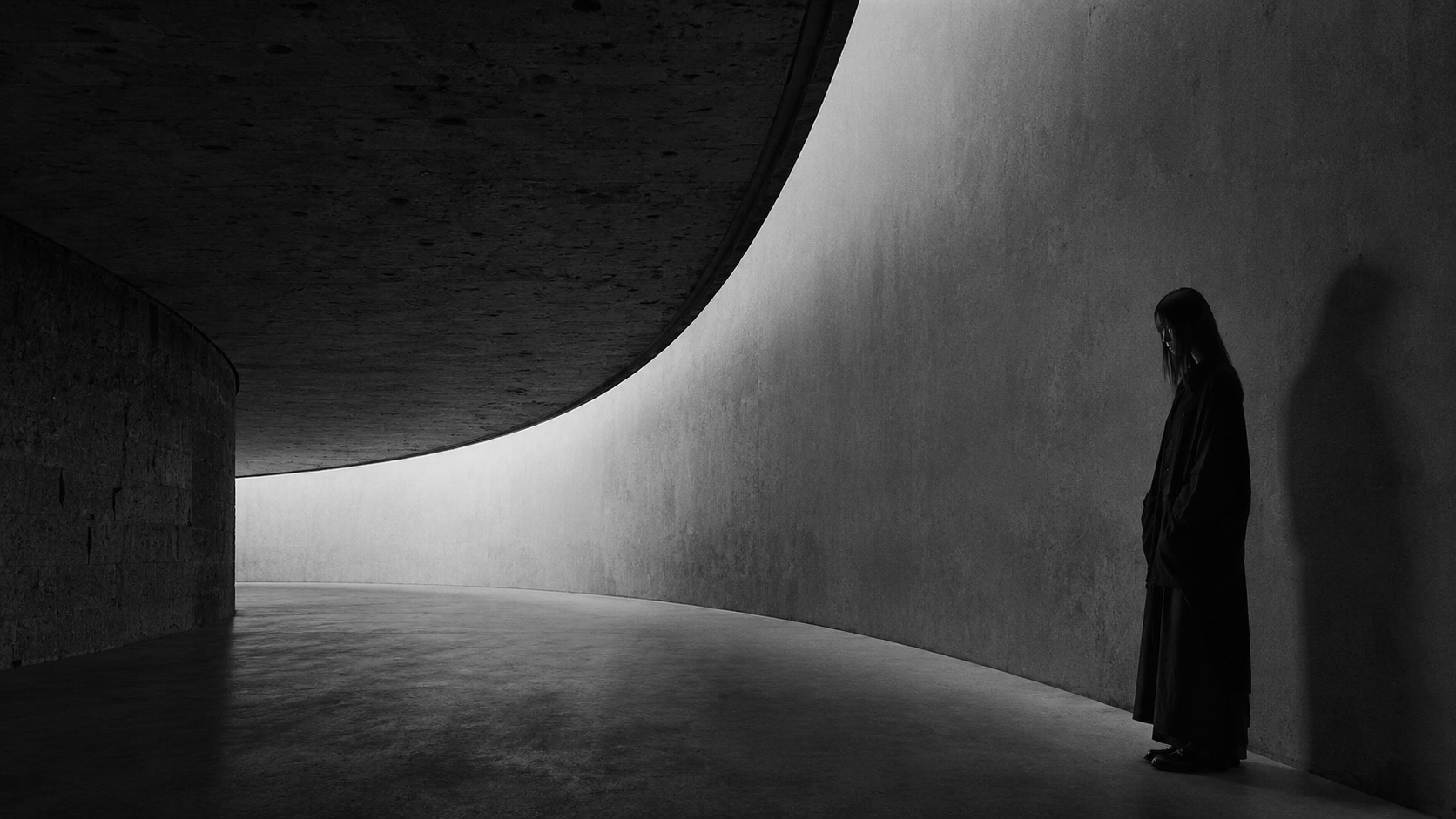 Monumental dark architectural interior with a solitary figure beneath a shaft of light